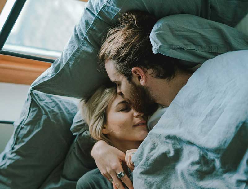 Young couple enjoying intimate moment together on couch with green pillows during low-key date night at home